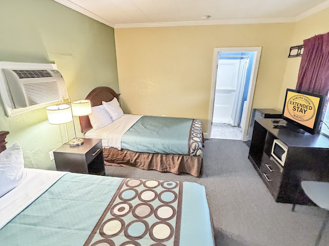 Guest room with two neatly prepared beds, television, and workspace